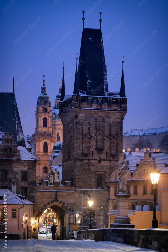 Lesser Town Bridge Tower during the moody winter night. Romantic scene before the sunrise with the snow and illuminated lamps.
