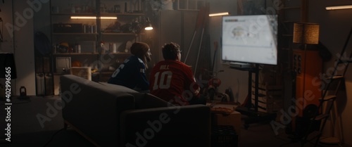 Two friends playing hockey sport video game inside garage hideout, enjoying pizza and drinks. TV screen is blurred