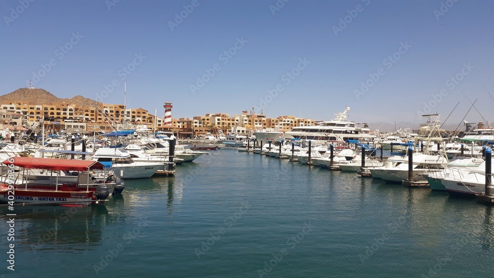 Marina with moored small boats and cityline with the lighthouse in the background in Cabo San Lucas, Mexico 