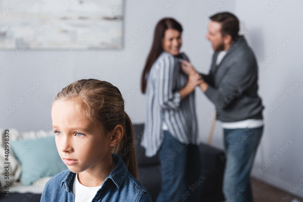 Upset kid standing near parents quarreling on blurred at home Upset kid standing near parents quarreling on blurred at home