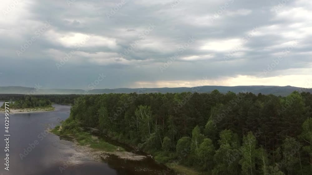 View of the river among green trees in cloudy cloudy weather. Beautiful wildlife of Siberia from the drone