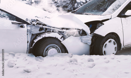 Close up view of a car crash on a snowy road in winter, where two white cars have been wrecked in a front collision