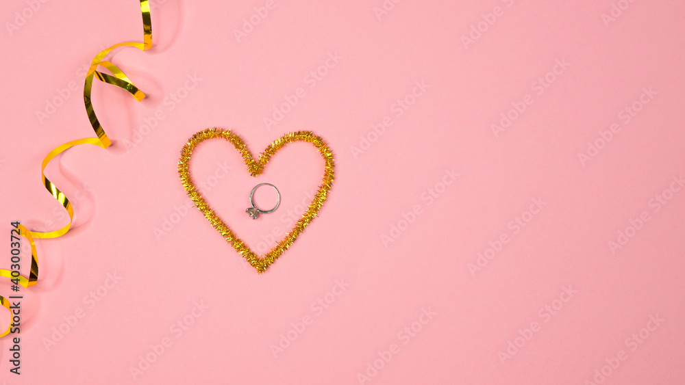 
Valentine's day top view flat lay. Engagement ring in shiny gold heart on pink paper background. Love romantic relationship concept. Copy space for text. Surprise gift for 14 February holiday 