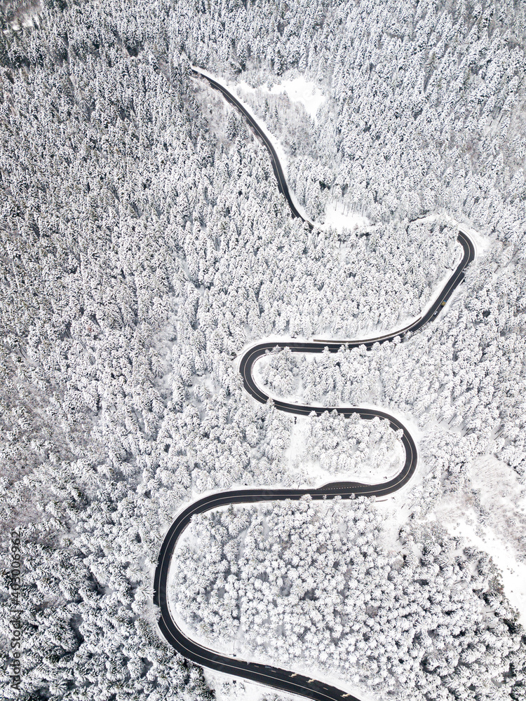 Winding road among a snowy forest, from high mountain pass, winter weather. Aerial view by drone. Romania