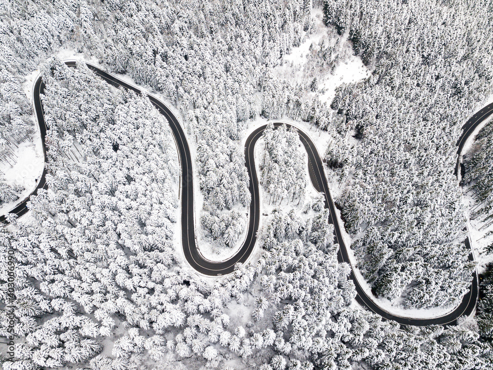 Winding road among a snowy forest, from high mountain pass, winter weather. Aerial view by drone. Romania