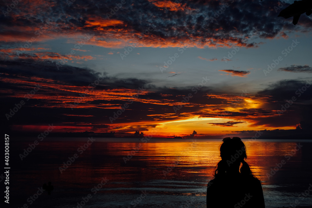 Woman contemplating a very colorful sunset on the beach in front of the sea