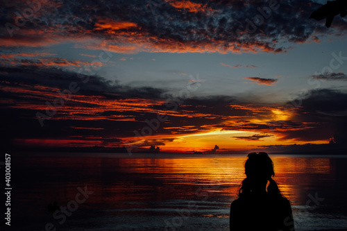 Woman contemplating a very colorful sunset on the beach in front of the sea
