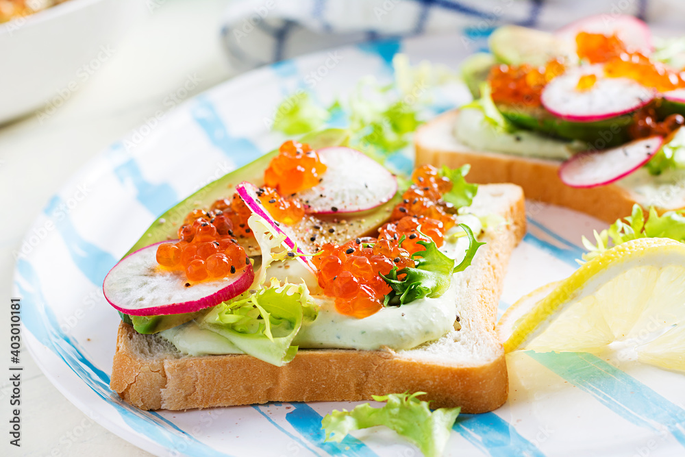 Sandwiches with salmon red caviar with sliced avocado and radish. Sandwich for lunch. Premium food Sandwiches with salmon red caviar with sliced avocado and radish. Sandwich for lunch. Premium food