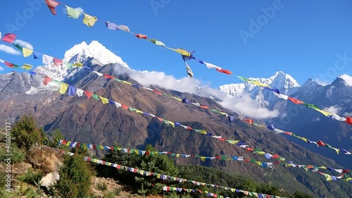 Several lines of colorful Buddhist prayer flags flying in the wind above Namche Bazar, Khumbu, Himalayas, Nepal with majestic mountain panorama in background including Thamserku peak (6,623 m).