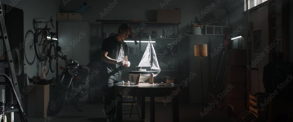 WIDE Caucasian teenager boy placing sails on his boat model school project inside his home garage. Shot with 2x anamorphic lens WIDE Caucasian teenager boy placing sails on his boat model school project inside his home garage. Shot with 2x anamorphic lens