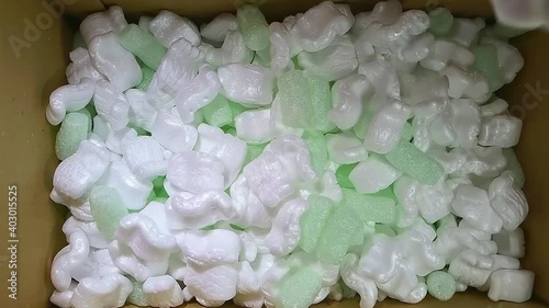 green foam rubber and white styrofoam chips filler falls into a cardboard box for packing, slow motion photo