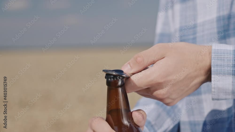Man opens a bottle of beer against the backdrop of a wheat field. Slow motion video