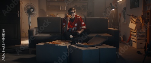 Canvas Print POV Portrait of Caucasian teenager playing video game inside home garage, enjoying pizza