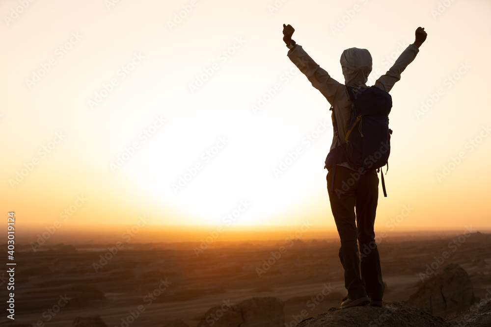Successful woman hiker open arms on sand desert in the sunset