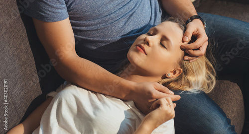 Close up photo of a caucasian woman with blonde hair lying on her lover's knees with closed eyes on the sofa