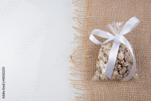 peanuts in kujut in a gift transparent package tied with a white ribbon on a burlap on a white background © Makulov
