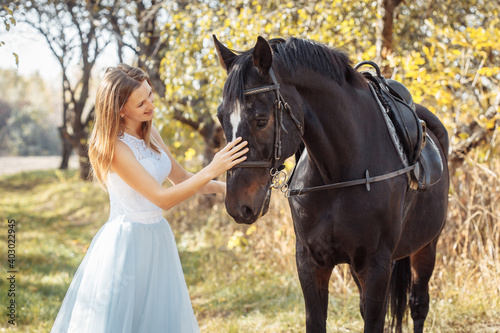 woman in white wedding dress walking with a horse in autumn park. horseback riding