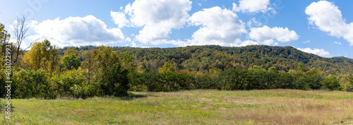Panoramic view of a low mountain landscape, green field with trees, blue sky with clouds, horizontal aspect