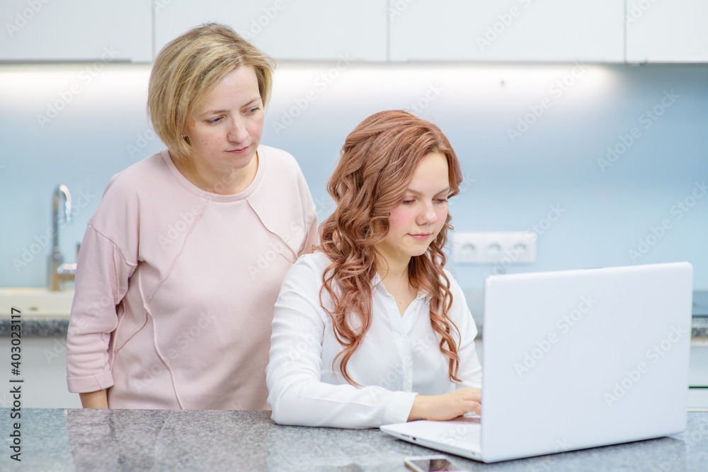 An adult daughter helps her mother figure out how to work with a laptop by pointing at the laptop screen.