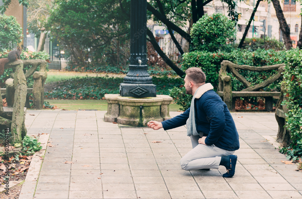 young man in park looking at a squirrel on a railing young man in park looking at a squirrel on a railing
