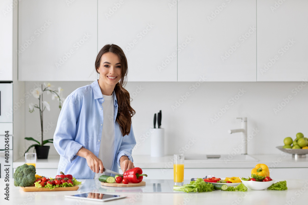 Young beautiful woman preparing a salad of fresh vegetables in a bright kitchen.