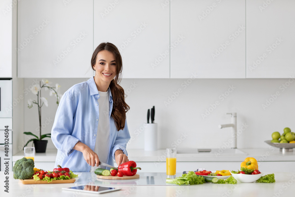 Young beautiful woman preparing a salad of fresh vegetables in a bright kitchen. Young beautiful woman preparing a salad of fresh vegetables in a bright kitchen.