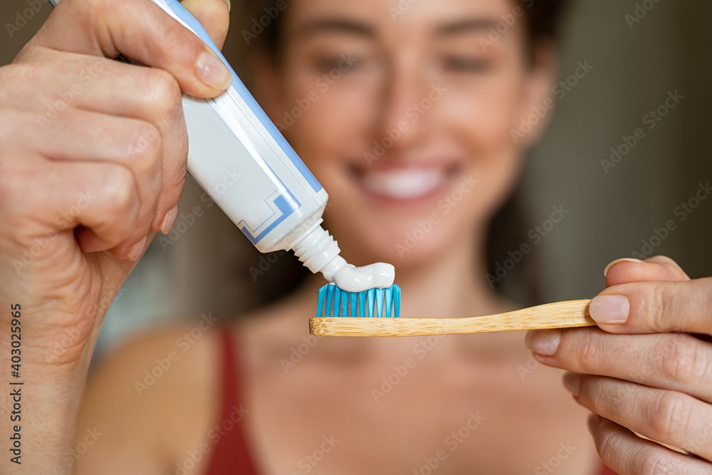 Woman applying toothpaste on bamboo toothbrush - obrazy, fototapety, plakaty 
