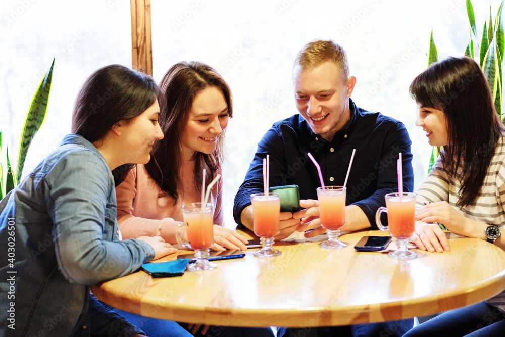 A guy and a girl at a table in a cafe are looking at a mobile phone - A group of young people is having fun in a bar and uses a smartphone - The concept of friendship, communication A guy and a girl at a table in a cafe are looking at a mobile phone - A group of young people is having fun in a bar and uses a smartphone - The concept of friendship, communication