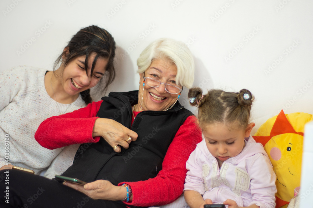 Little cute girl and her grandmother and sister are spending time together at home. Having fun, hugging and smiling while sitting on sofa.