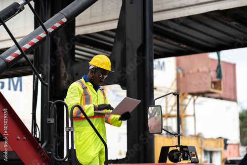 engineer man / worker in safety jumpsuit uniform with yellow hardhat and use laptop computer control at cargo container ship port warehouse.transport import,export logistic industrial service