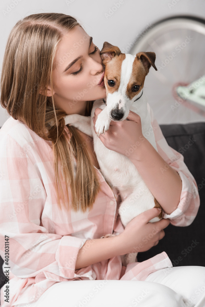 young woman holding in arms and kissing jack russell