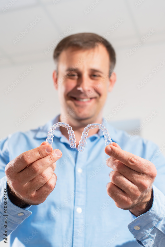 Fototapeta premium A smiling dentist doctor holds transparent aligners in his hands