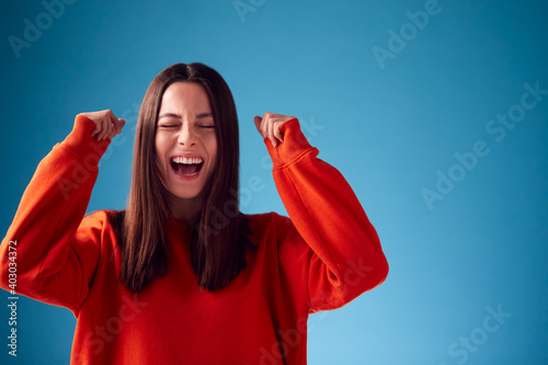 Excited Young Woman Celebrating And Pumping Fists In The Air Against Blue Studio Background photo