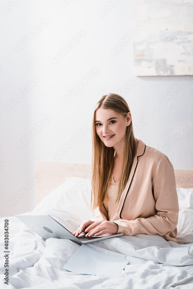 cheerful young freelancer in silk robe using laptop in bedroom cheerful young freelancer in silk robe using laptop in bedroom