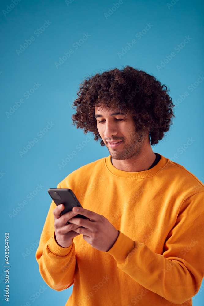 Studio Portrait Of Young Man Looking At Mobile Phone Against Blue Background Studio Portrait Of Young Man Looking At Mobile Phone Against Blue Background