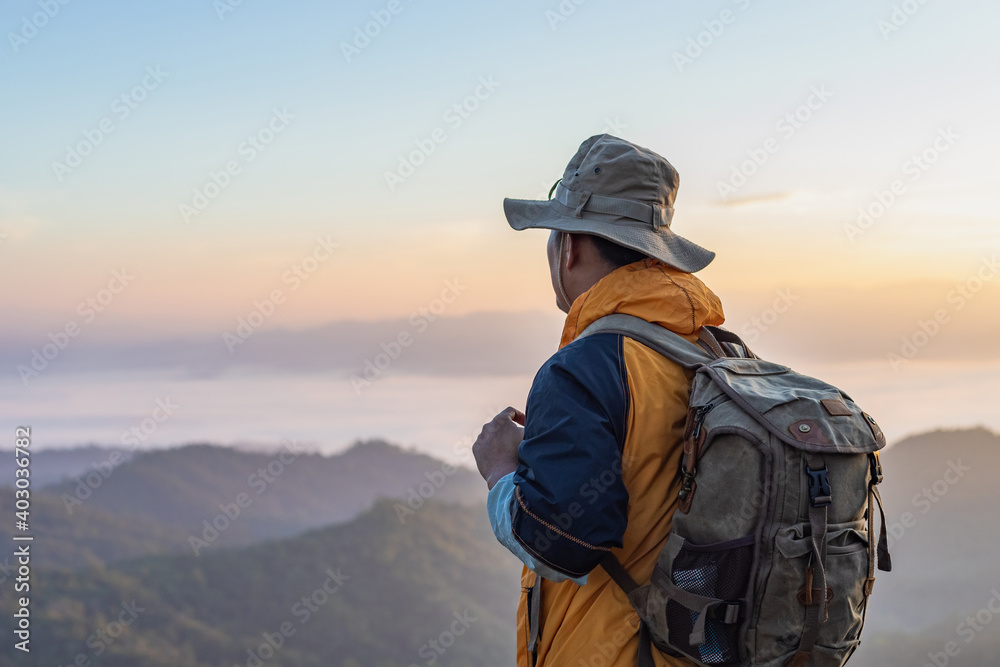 Hipster male hiker with backpack enjoying sunset on peak of foggy mountain. Tourist traveler on background view mockup. - obrazy, fototapety, plakaty 