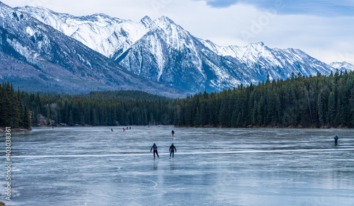 Tourists doing ice-skating in Johnson Lake frozen water surface in winter time. Snow-covered mountain in the background. Banff National Park, Canadian Rockies, Alberta, Canada.