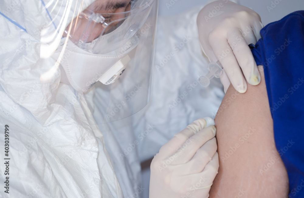 Fototapeta premium Doctor or nurse wearing ppe suit, mask, face shield and injection covid 19 vaccine to patient at upper arm. Doctor injection vaccine for stimulating the body to build immunity against COVID-19.