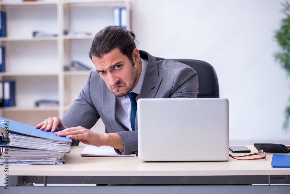 Young male employee unhappy with excessive work in the office Young male employee unhappy with excessive work in the office