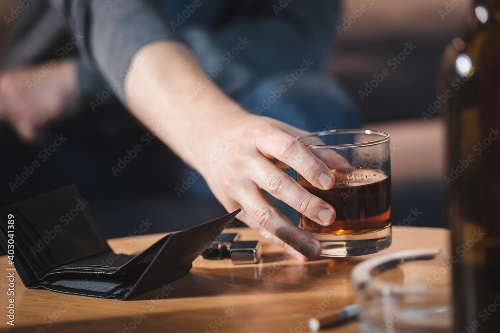 selective focus of addicted man taking glass of whiskey near empty wallet on blurred foreground