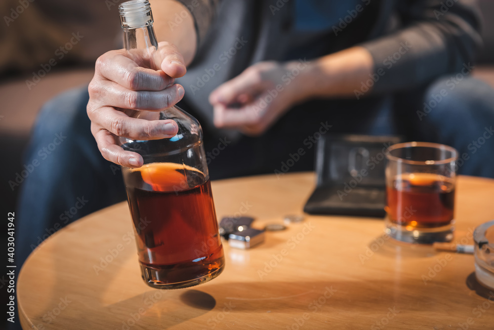 partial view of alcohol-addicted man holding bottle of whiskey, blurred background partial view of alcohol-addicted man holding bottle of whiskey, blurred background