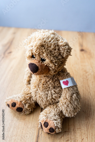 Ein brauner Teddybär mit einem Pflaster und einem Herz darauf am Arm. Impfung, Gesundheit. Holz Tisch, Nahaufnahme.