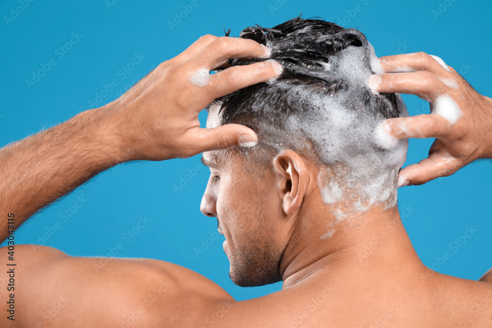 Handsome man washing hair on light blue background, back view Handsome man washing hair on light blue background, back view