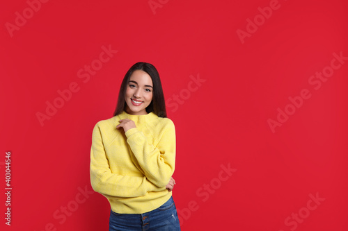 Beautiful young woman wearing yellow warm sweater on red background. Space for text