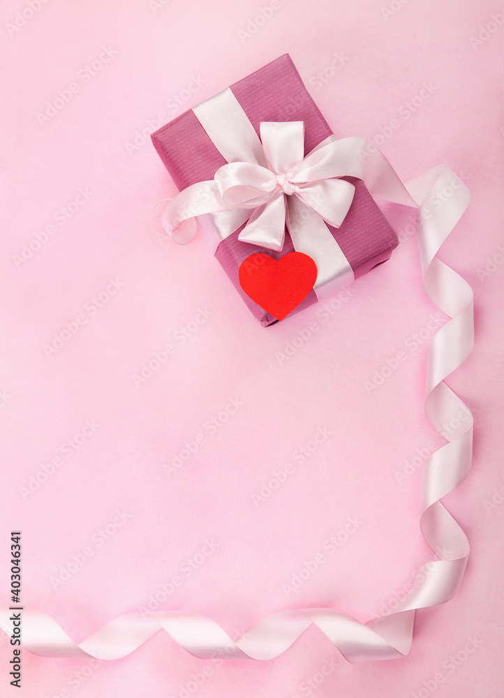 Pink gift box, white bow, long curved ribbon, paper red heart and empty space for text. Top view, flat lay. Valentines Day, Wedding day, birthday, Mothers Day greeting background or invitation