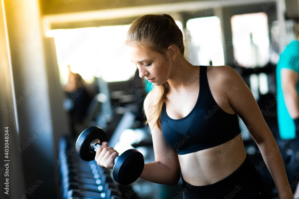 Exercising, Gym, fitness Women concept. athletic young woman doing a fitness workout with dumbbells at indoor gym Exercising, Gym, fitness Women concept. athletic young woman doing a fitness workout with dumbbells at indoor gym