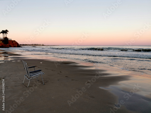 A beach chair on the sand against the ocean in the evening. © Galina