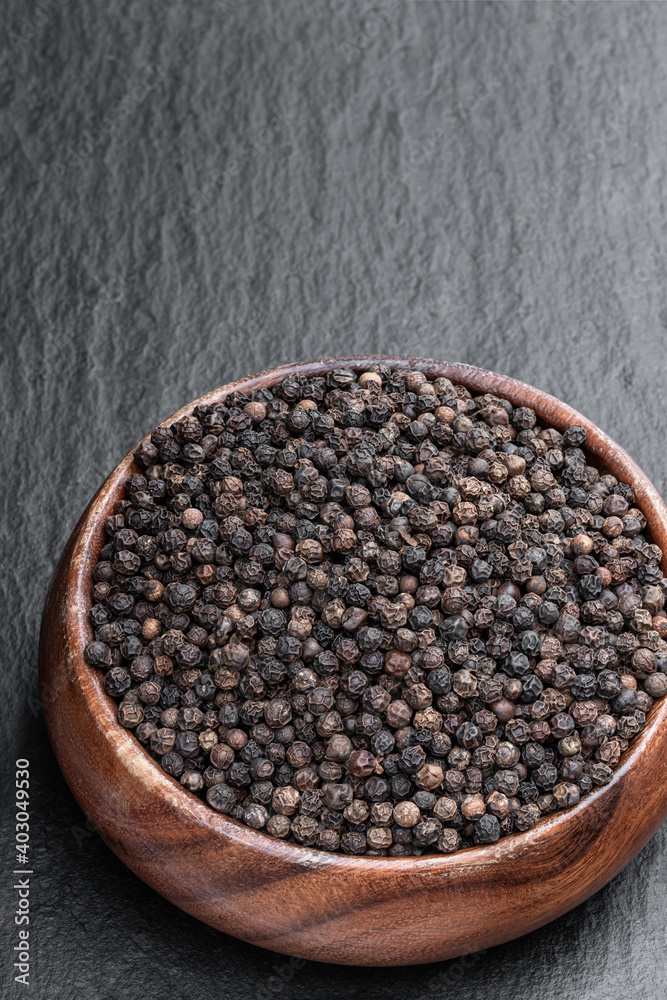 Black pepper corn in wooden bowl on black stone background Black pepper corn in wooden bowl on black stone background