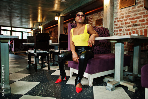 Stunning African American women in yellow top and black leather pants pose at pub.