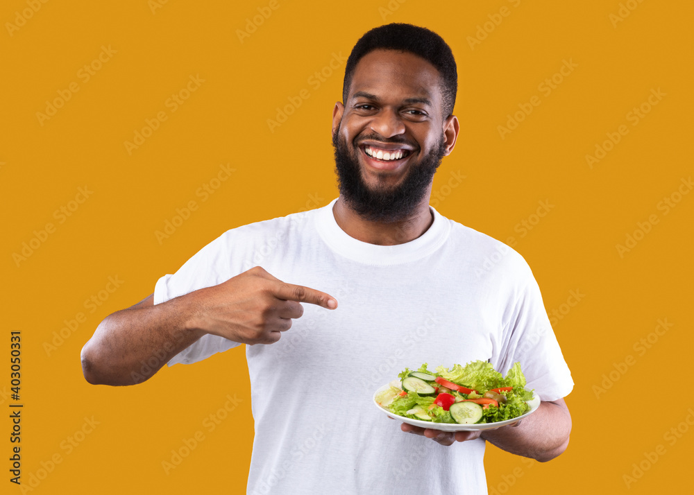 African Man Pointing Finger At Salad Standing On Yellow Background African Man Pointing Finger At Salad Standing On Yellow Background